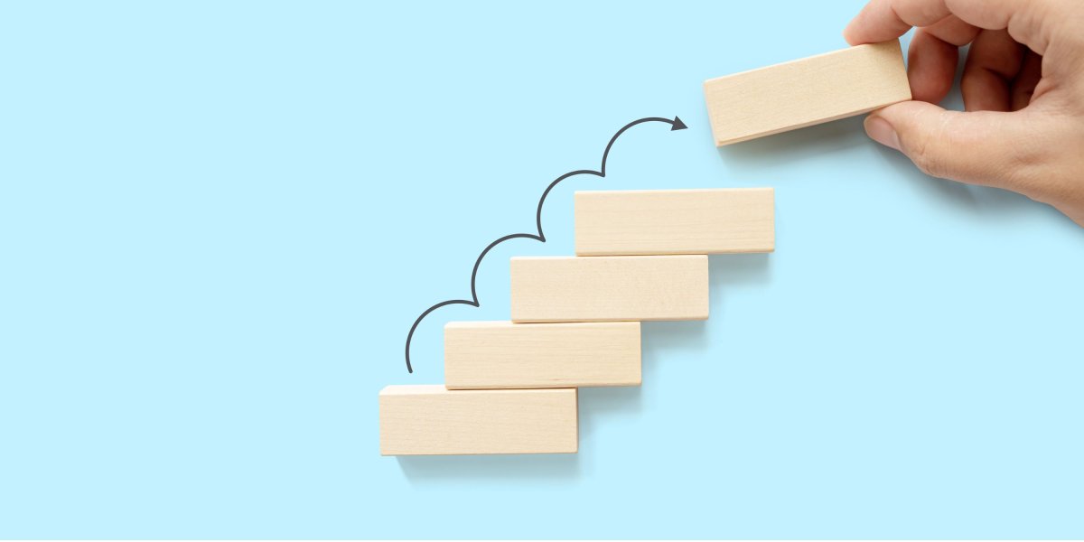 Wooden blocks in a step formation and an arrow jumping up to the top