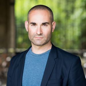 Photograph of Dr Ben Crewe, wearing a blue t shirt and blue suit jacket.