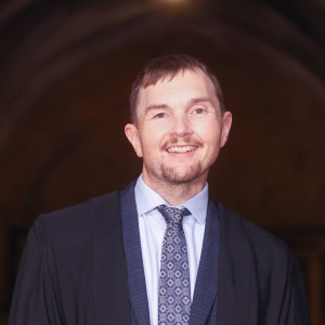 Photograph of Nic Lane in a dark blue gown and blue tie