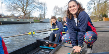 A College rower smiles beside their crew on the river.
