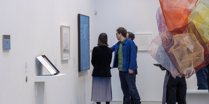Two people standing in a gallery space looking at artworks hanging on the wall.