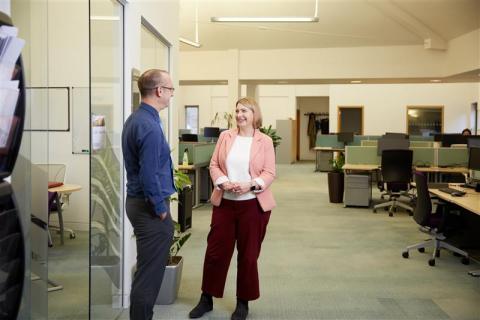 Two people standing and talking in an open plan office