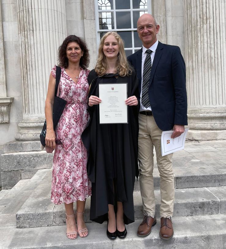 Hannah Clayton holding her graduation certificate on the steps of Senate House