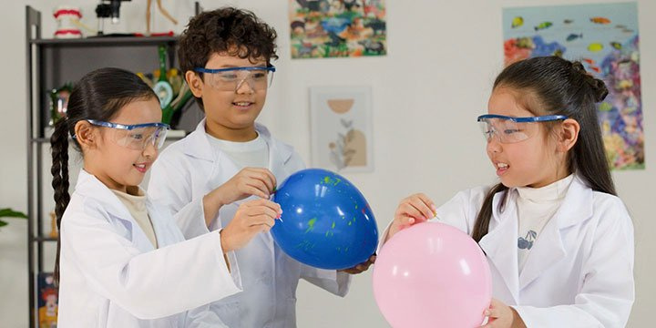 Children wearing lab coats doing a science experiment involving balloons