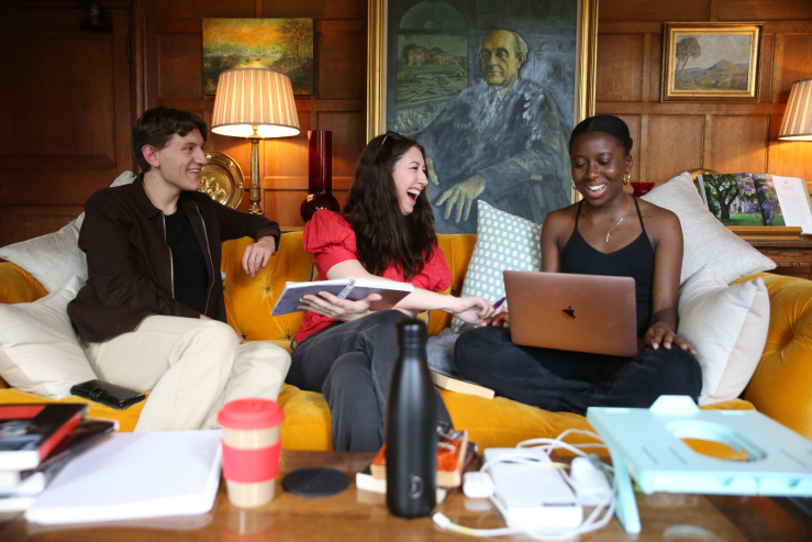 Students laughing and holding studying materials on a sofa