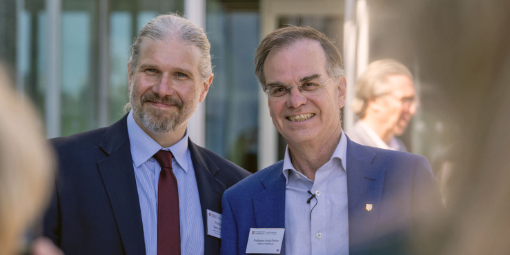 Professor Mete Atatüre and Professor Andy Parker  smiling at an outdoor event, one wearing a red tie and the other a blue tie, b