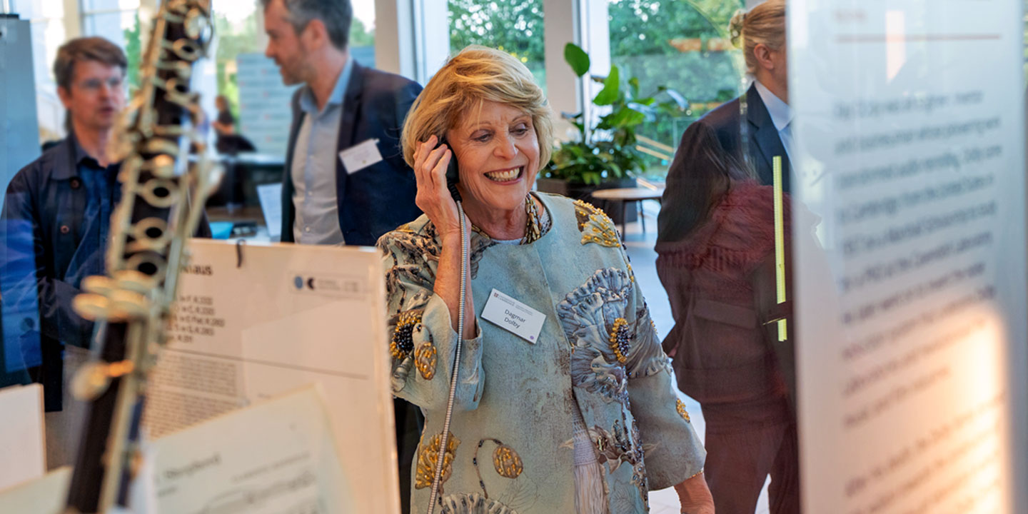 Dagma Dolby smiling while using a listening device at an indoor exhibition with other attendees in the background.