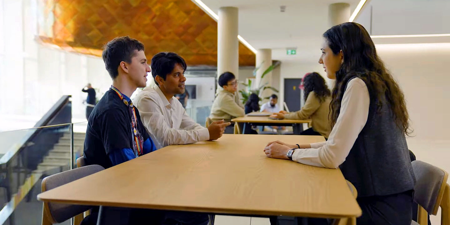 Three people engaged in a discussion at a table in a modern, brightly lit indoor setting.