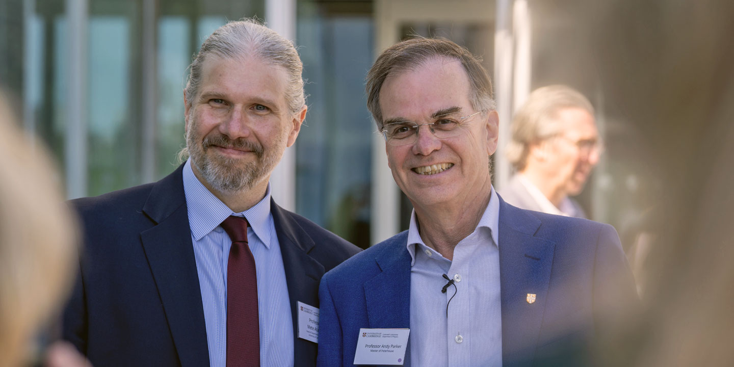 Professor Mete Atatüre and Professor Andy Parker  smiling at an outdoor event, one wearing a red tie and the other a blue tie, both in business suits.
