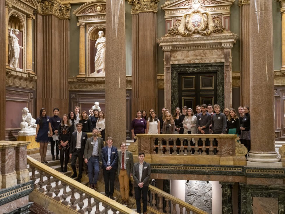 Wolfson scholars at the Fitzwilliam Museum, Cambridge, 2019. A group of approximately 50 people stand on a staircase and balcony in the grand foyer of the Fitzwilliam Museum.