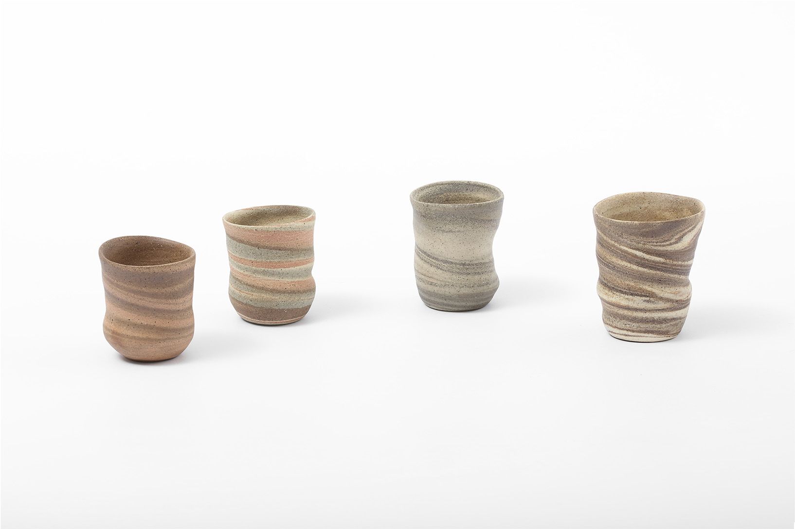 Four small hand‑formed ceramic cups arranged in a row on a white background, each with softly uneven shapes and horizontal marbled bands in muted earthy tones.