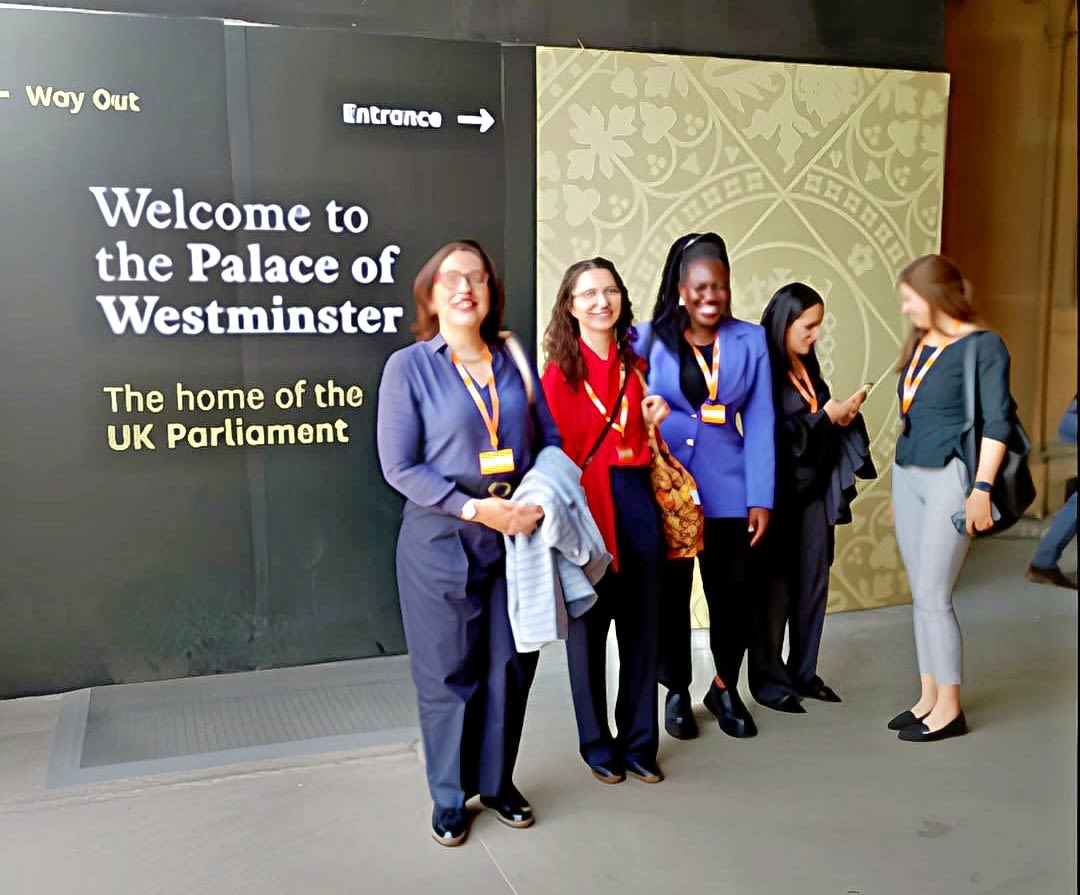 Photograph of the The FibroidsFree, Cambridge team stood in front of a printed banner at the Palace of Westminster