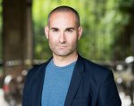 Photograph of Dr Ben Crewe, wearing a blue t shirt and blue suit jacket.