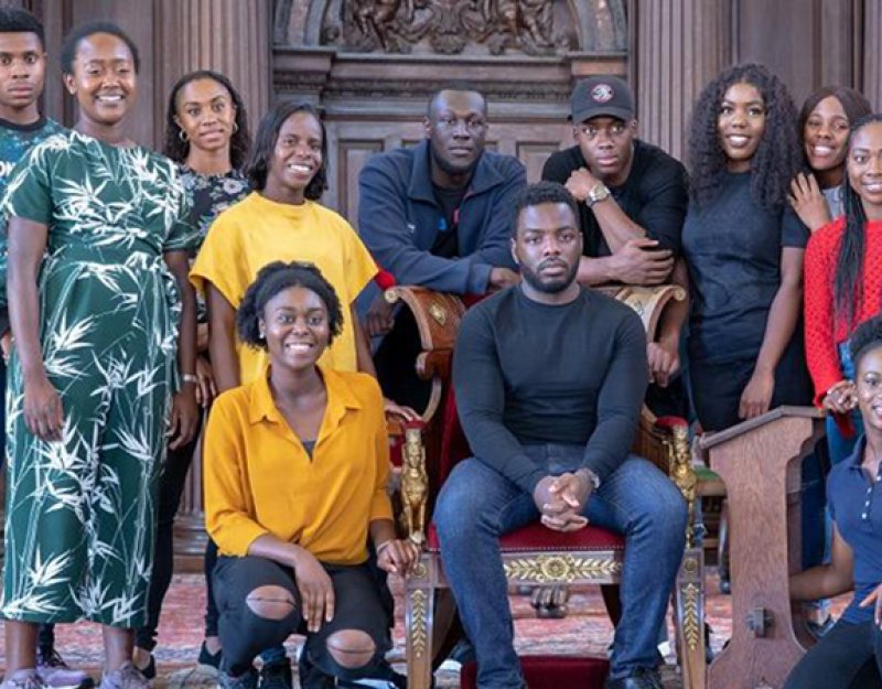 Stormzy seated and surrounded by students from the University of Cambridge Afro-Caribbean Society