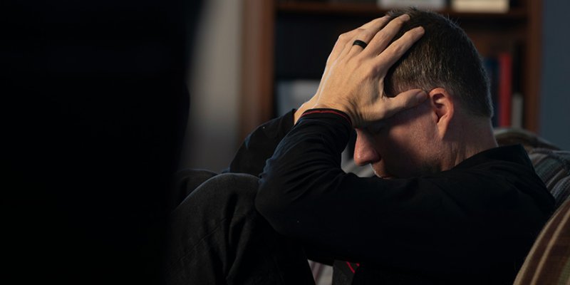 A man sitting on a couch holding his head in his hands