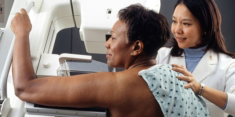 Female doctor standing near woman patient doing breast cancer scan