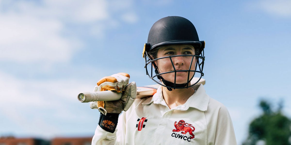 Holly Tasker in her cricket uniform and holding a cricket bat over her shoulder