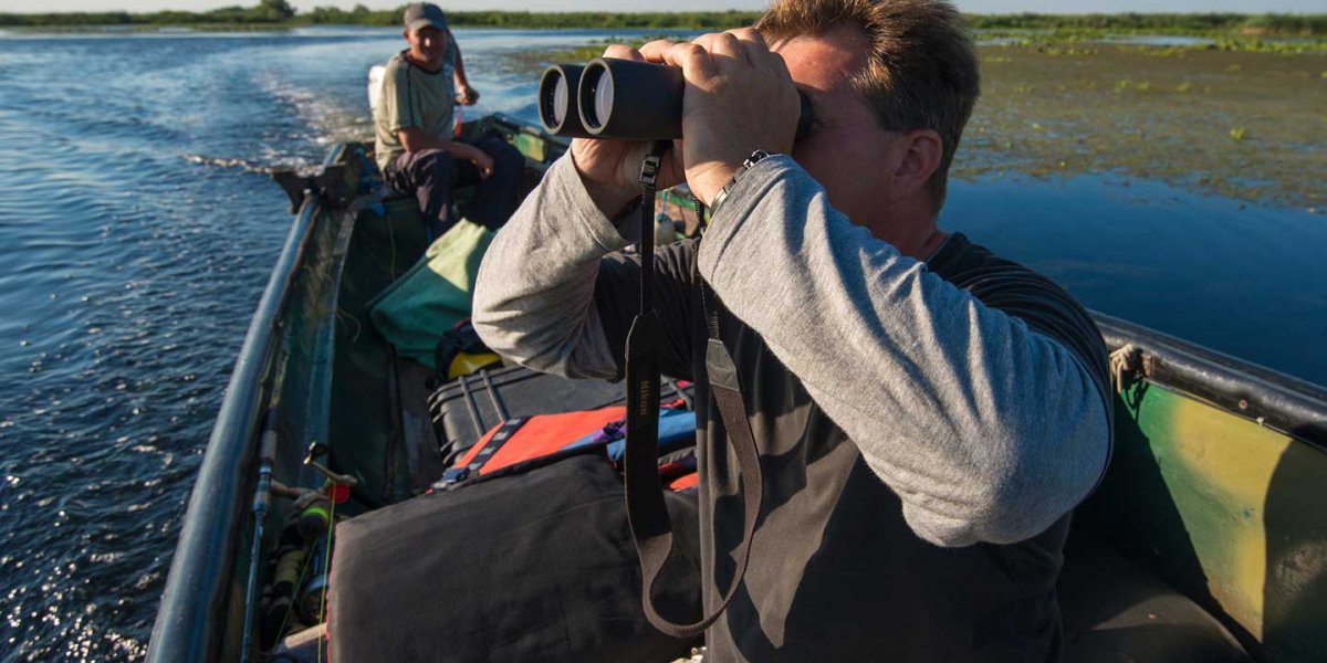 Rewilding Europe. Man in a speedboat looking left through binoculars.
